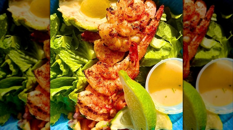 close-up of seasoned shrimp over a salad with avocado and lime