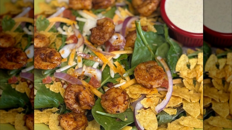 close-up of a salad with shrimp, spinach, shredded cheese, onions, and crumbled tortilla chips