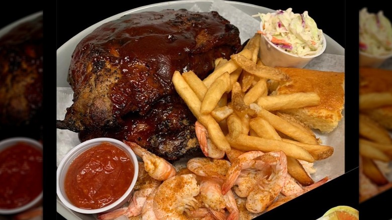 A platter of shrimp, fries and meat with dipping sauce, slaw, and cornbread