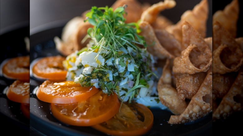 close-up of scallop ceviche on a plate with sliced tomatoes and fried wontons