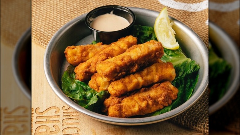 Fried mahi fingers with dipping sauce on a metal plate atop a wood table