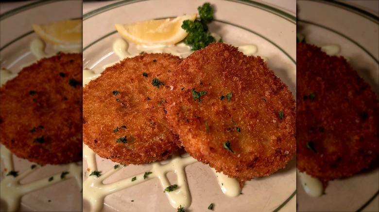 Crab and shrimp cakes on a plate, with sauce and a lemon.
