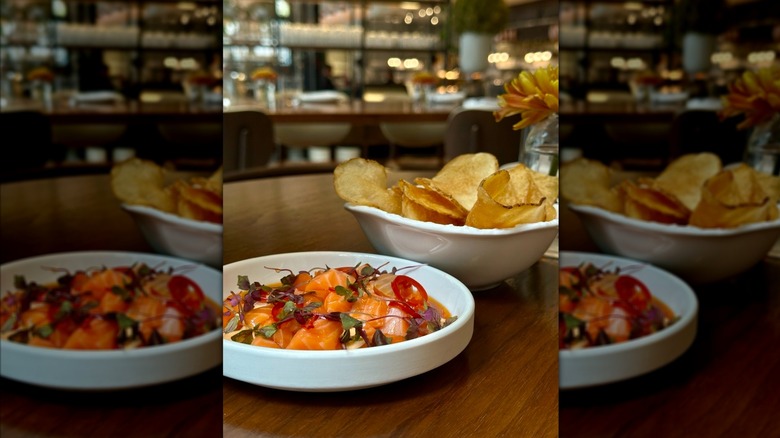 A plate of salmon ceviche and bowl of potato chips with Vernick Fish's interior in the background