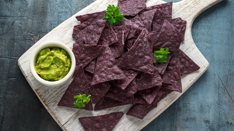 Blue corn tortilla chips on cutting board with bowl of guacamole