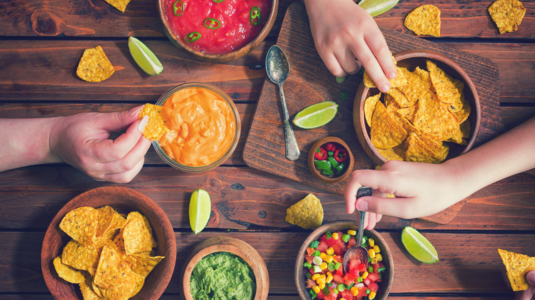 Overhead view of people eating tortilla chips with assorted dips