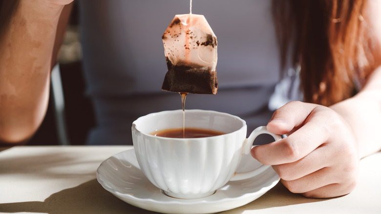 Woman removing tea bag from hot cup of tea