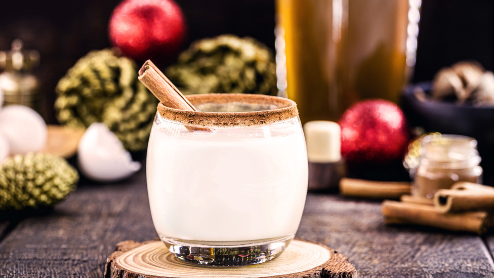 glass of eggnog with Christmas decorations in background