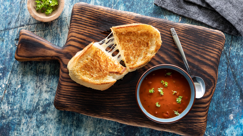 A bowl of tomato soup and a grilled cheese sandwich on a wooden cutting board.