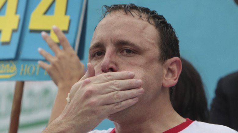 Joey Chestnut with hand over mouth in eating contest