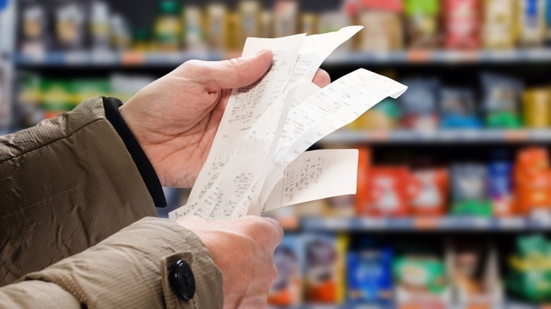 Hands holding receipts in grocery store aisle