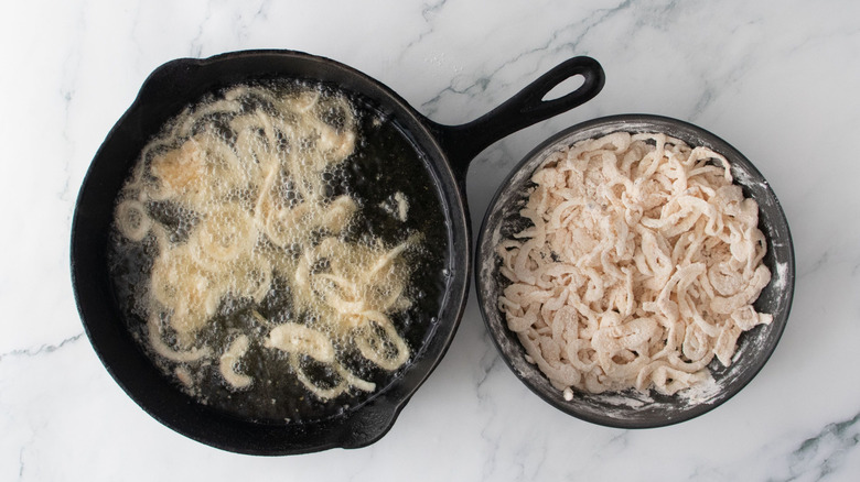 Onions frying in cast iron skillet next to bowl of unfried onions