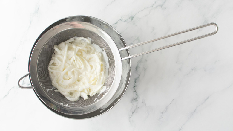 Buttermilk coated sliced onions draining in bowl