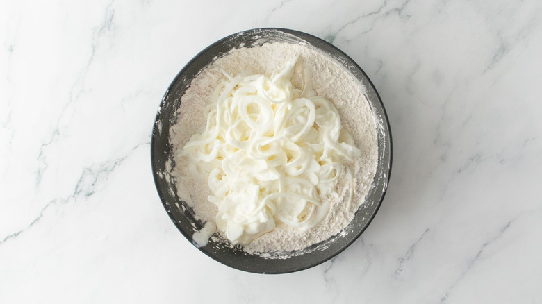 Sliced onions sitting in flour mixture in bowl