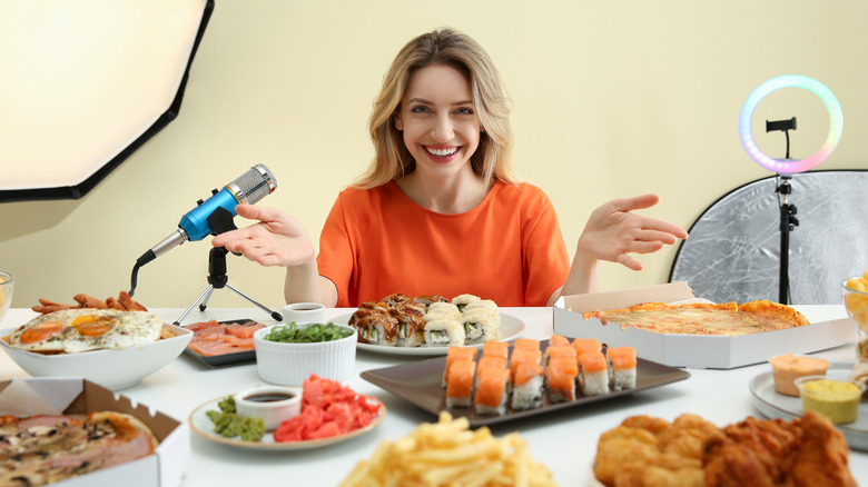 a woman sitting at the table surrounded by lots of food and her microphone, lighting and screen for asmr