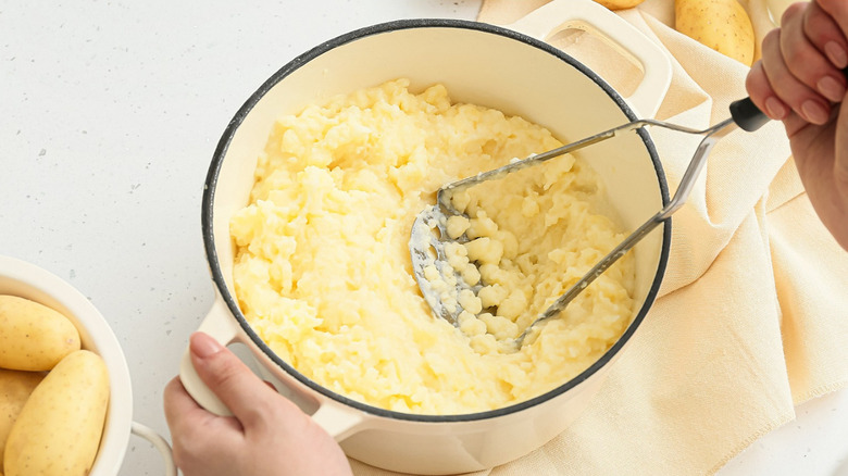 potatoes being mashed in white pot