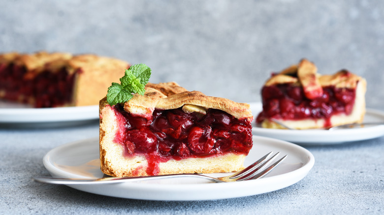Slice of cherry pie on white plates on a table with fork
