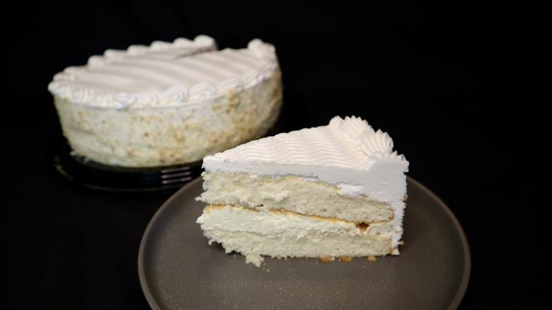 A slice of vanilla cake on a plate with a full cake in the background
