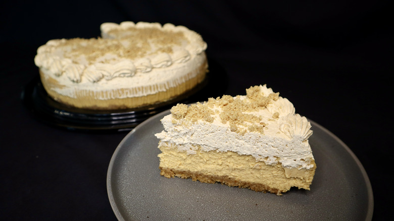 A pumpkin cheesecake slice on a plate with a full cheesecake behind