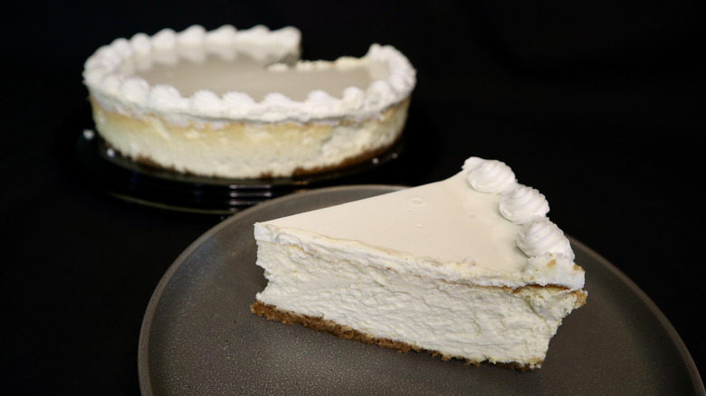 A slice of Costco cheesecake on a plate with a full cheesecake in the background