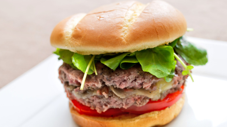 Sous vide burger in a bun with a tomato slice and baby spinach leaves