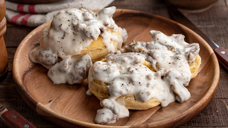 Biscuits and sausage gravy on wooden plate.