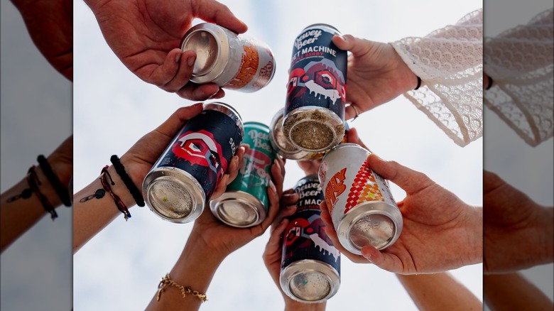Picture taken from below hands clinking dewey beer company beer cans