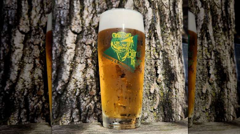 A pint of beer with a logo of a tiger with no eyes and a triangle in the colors green and yellow. The logo reads: Blind tiger Brewery and restaurant