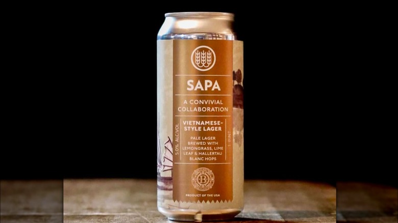 A beer can with a golden brown design that reads: sapa, a convivial collaboration, vietnamese-style lager, pale lager brewed with lemongrass, lime leaf and hallertau blanc hops, product of the USA