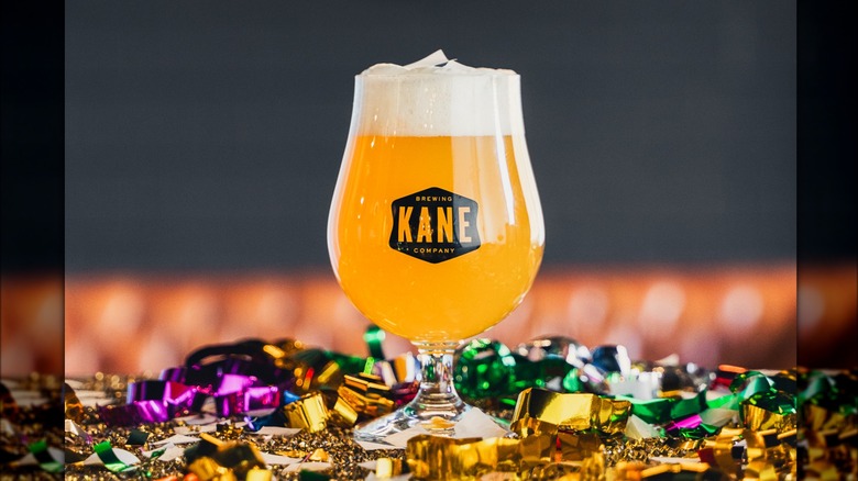 A glass of Kane Brewing company filled with beer, on top of a table covered in metallic confetti