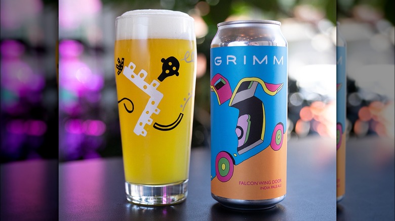 A pint of beer with a black and white line-art drawing of a character with a face and a tail, alongside a can of beer with a light blue and orange background and an artistic design of what it looks like to be a falcon car with the door open. The can reads "grimm, falcon wing door, india pale"