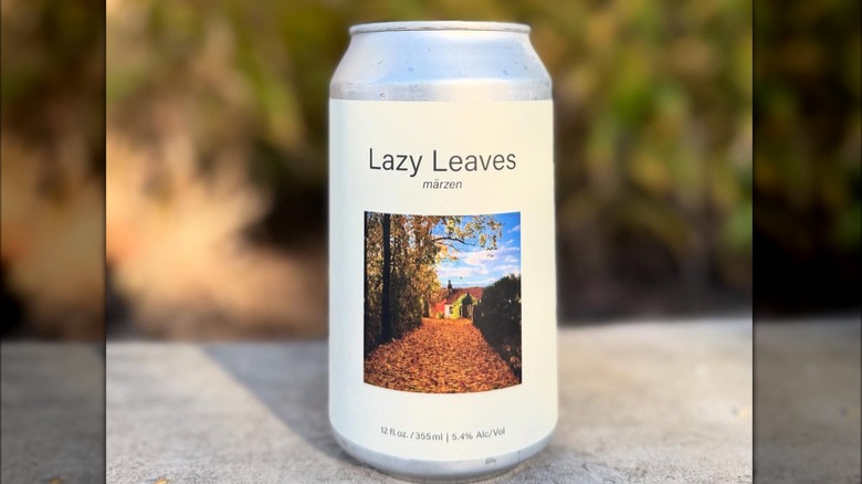 A can of Lazy leaves Märzen, with a white label with a picture of a house an a path filled with autumn leaves in the middle