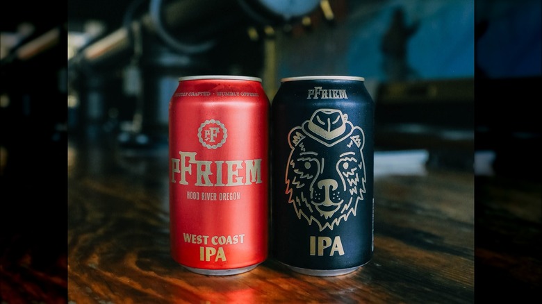 2 cans of beers. On the left, a red can with golden letters that read pFriem Hood River Oregon West coast IPA. On the right, a black can that reads pFriem IPA, with a design of a bear wearing a hat
