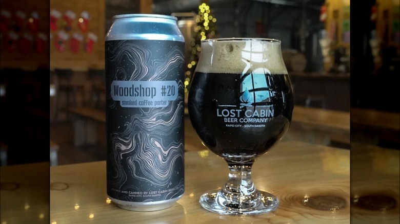 On the left, a can of Woodshop #20 smoked coffee porter. on the right, A lost cabin beer company glass full of beer