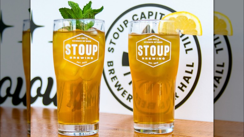 Two beer glasses, one with mint on top, the other with a lemon slice. Both glasses read" the art & science of beer Stoup Brewing est. 2013"