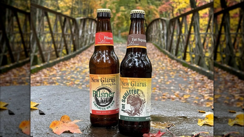 Two beer bottles. The one on the right has a yellow and red design, and reads: "New Glarus Pilsner, employee owned". The one on the right, yellow and green, reads: New Glarus Fat Squirrel.