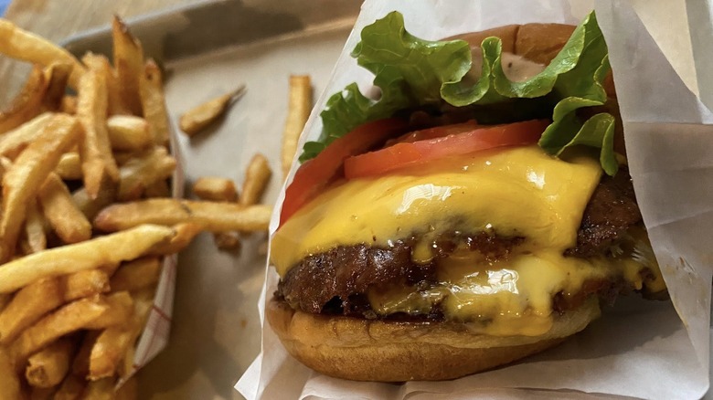 Smash double cheeseburger with lettuce and tomato in paper wrapper next to tray of fries