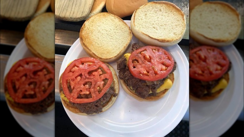 two open faced cheeseburgers on toasted buns with slices of heirloom tomatoes