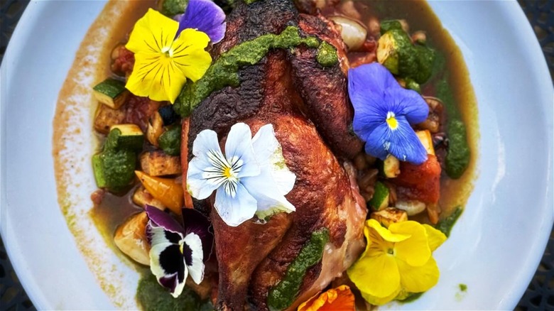 Half roast chicken in sauce garnished with edible flowers on a white plate at Toups' Meatery
