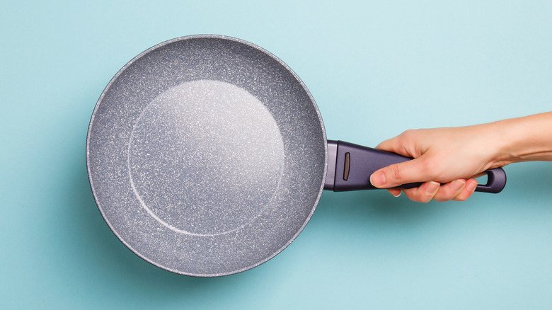 hand holding ceramic coated pan against blue background