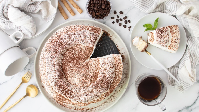 Tiramisu cheesecake next to slice on plate, coffee beans, and cup of coffee