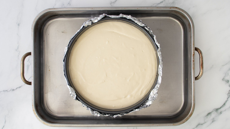 Cheesecake in pan surrounded by roasting pan filled with water