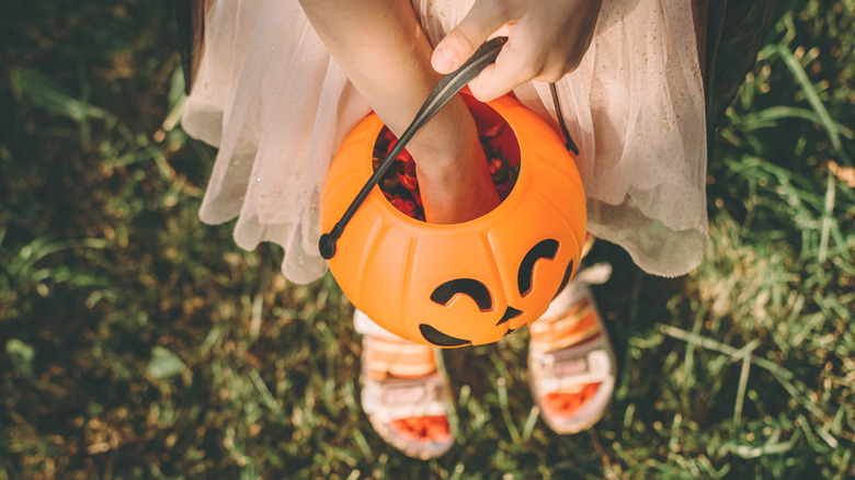 Child reaching into Halloween pumpkin bucket
