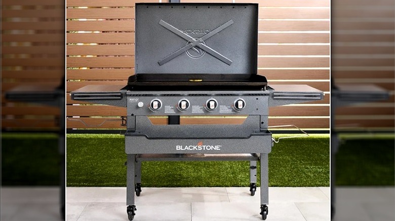 Blackstone outdoor grill with lid open in front of wood slats and green turf.