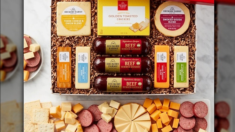 An open Hickory Farms gift box with meats and cheeses. Sliced cheese and meats with crackers sit in front of the gift box.