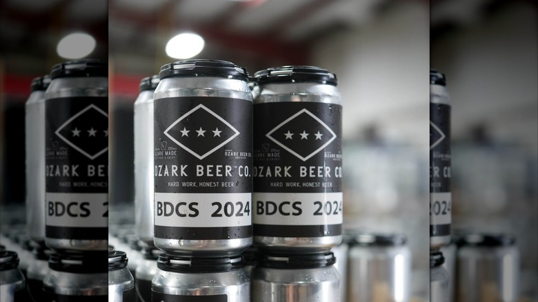 Stacked silver cans of Ozark Beer Co.'s BDCS 2024  in a brewery.