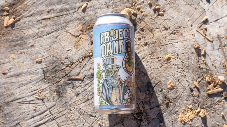 A can of Project Dank IPA resting on a weathered tree stump, surrounded by scattered wood chips