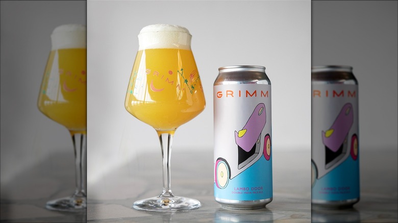 A can of Grimm Artisanal Ales' Lambo Door beside a stemmed glass filled with hazy golden beer topped with a thick foamy head