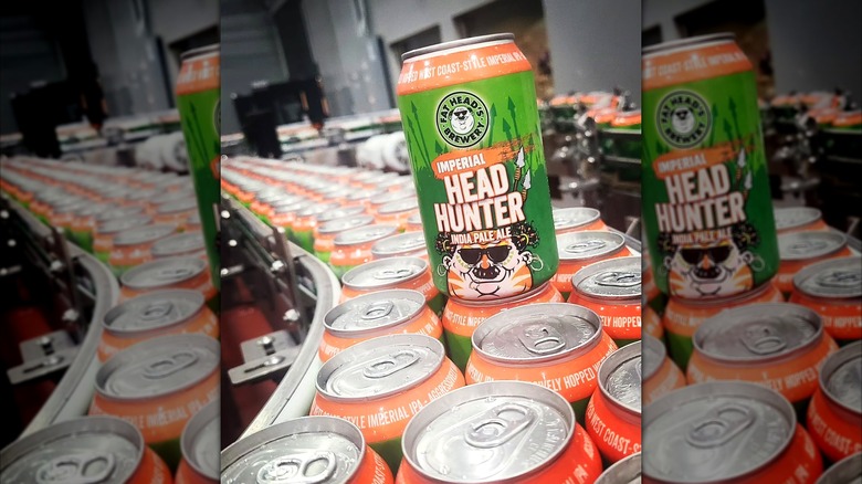 A single can of Fat Head's Imperial Head Hunter IPA on a canning line, surrounded by rows of matching green and orange cans inside a brewery