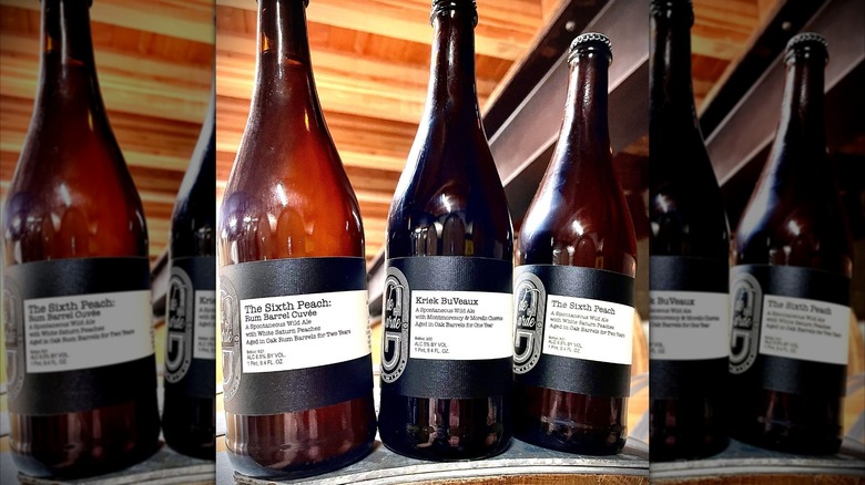 Three bottles of de Garde Brewing's wild ales on a wooden barrel