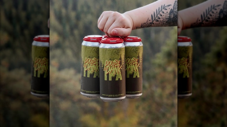 A tattooed hand holding a four-pack of Lost Cabin's Double So Dank IPA.